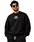 A man wearing a black Balenciaga crewneck sweatshirt and matching black sweatpants with white drawstrings, posed against a dark gray studio background.