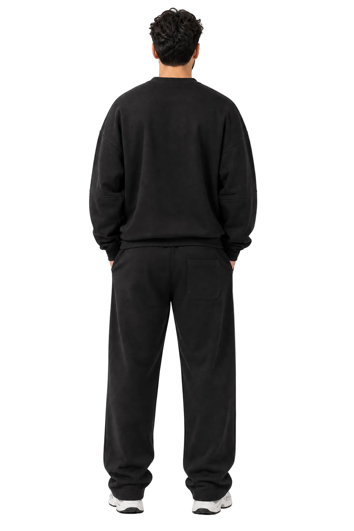 A man viewed from behind wearing a black crewneck sweatshirt and matching black sweatpants, standing against a plain light gray studio background.