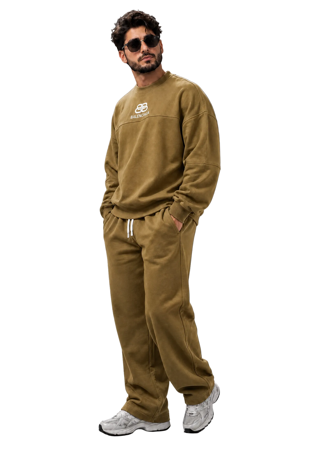 A man wearing a matching olive-brown sweatshirt and sweatpants set with white sneakers, standing against a dark gray studio background.