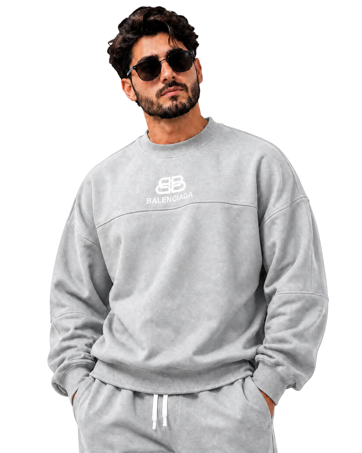 A man wearing a light gray Balenciaga crewneck sweatshirt and matching sweatpants, styled with sunglasses, against a dark gray textured studio background.