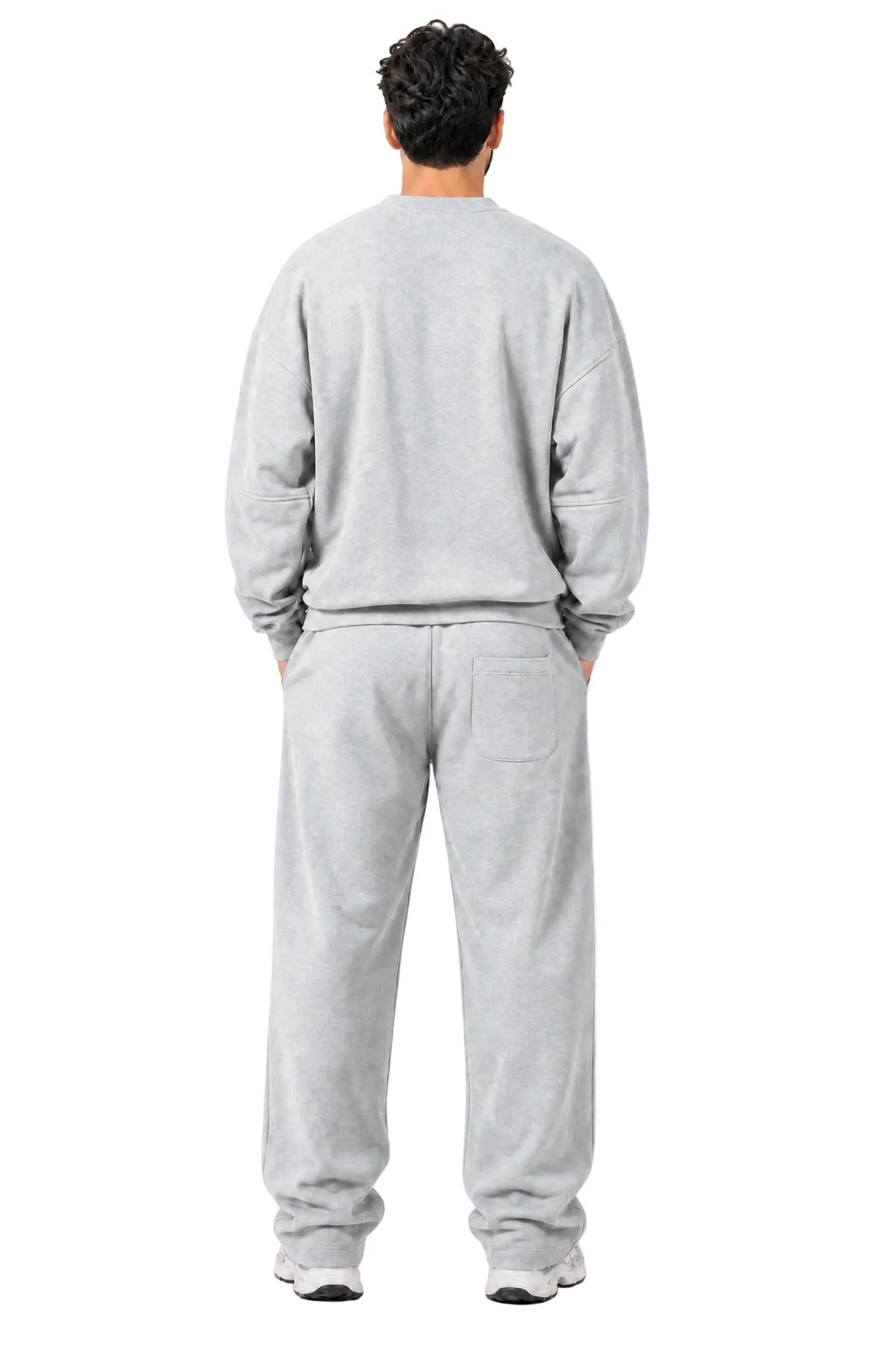 A man viewed from behind wearing a light gray crewneck sweatshirt and matching light gray sweatpants, standing against a light gray textured studio background.