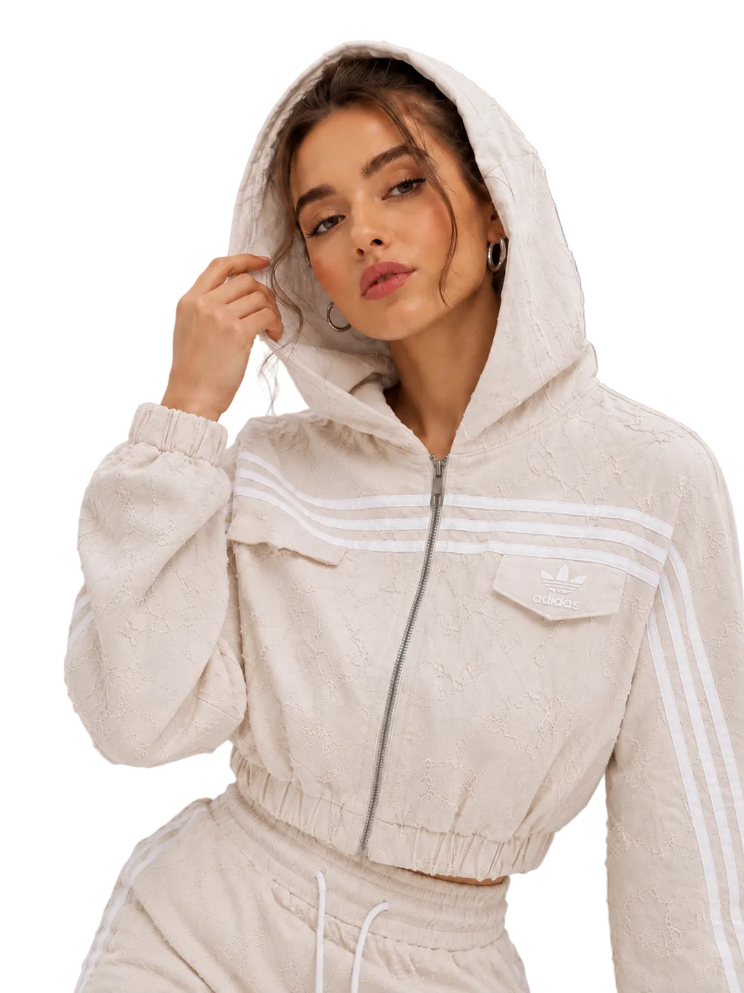 A woman wearing a beige textured zip-up hooded jacket with white stripes on the sleeves and chest, paired with matching beige joggers, against a neutral gray background.