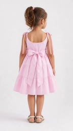 The back showcases a charming open-back-inspired design with adjustable tie shoulder straps and a decorative oversized bow at the waist, adding a refined finishing touch. The tiered skirt continues seamlessly around the garment, creating a balanced and flowing silhouette. The thoughtful details and comfortable fit make this dress both stylish and practical for young girls.