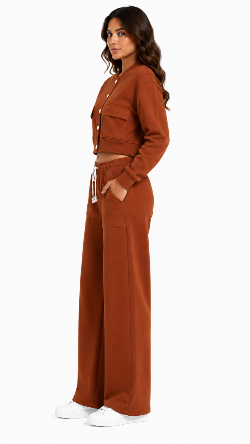إطلالة جانبية لطقم نسائي باللون الطوبي يضم جاكيت كروب بأكمام طويلة وبنطلون واسع بقصة مستقيمة مع جيوب جانبية ورباط خصر أبيض يمنح مظهراً كاجوال أنيقاً.