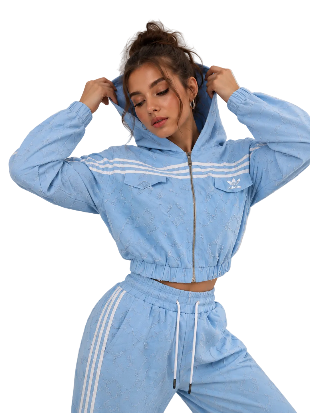 A woman modeling a light blue cropped zip-up hoodie and matching jogger pants set with white stripes, photographed against a plain light gray studio background.
