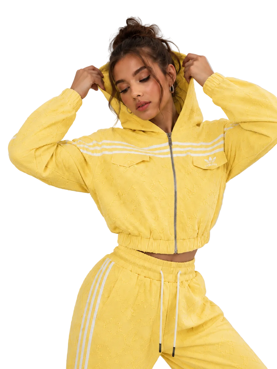 A woman modeling a bright yellow cropped zip-up hoodie and matching jogger pants set with white stripes, photographed against a plain light gray studio background.