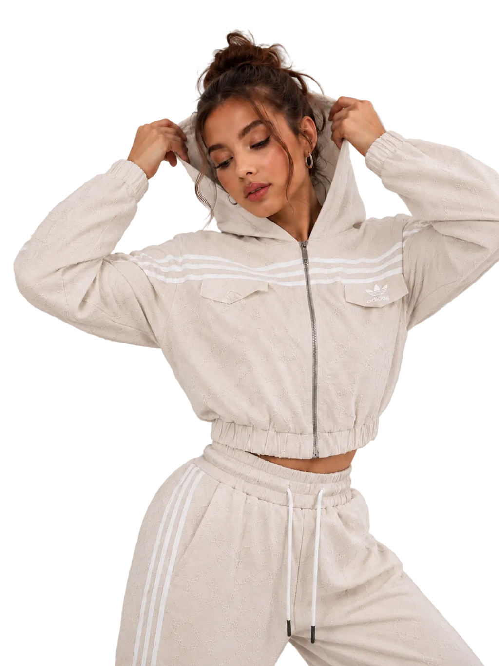 A woman modeling a light beige cropped zip-up hoodie with white stripes and matching jogger pants against a neutral gray studio background.