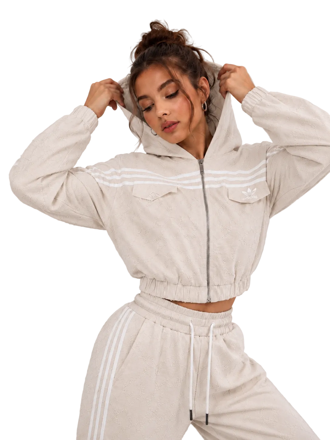 A woman modeling a light beige cropped zip-up hoodie with white stripes and matching jogger pants against a neutral gray studio background.
