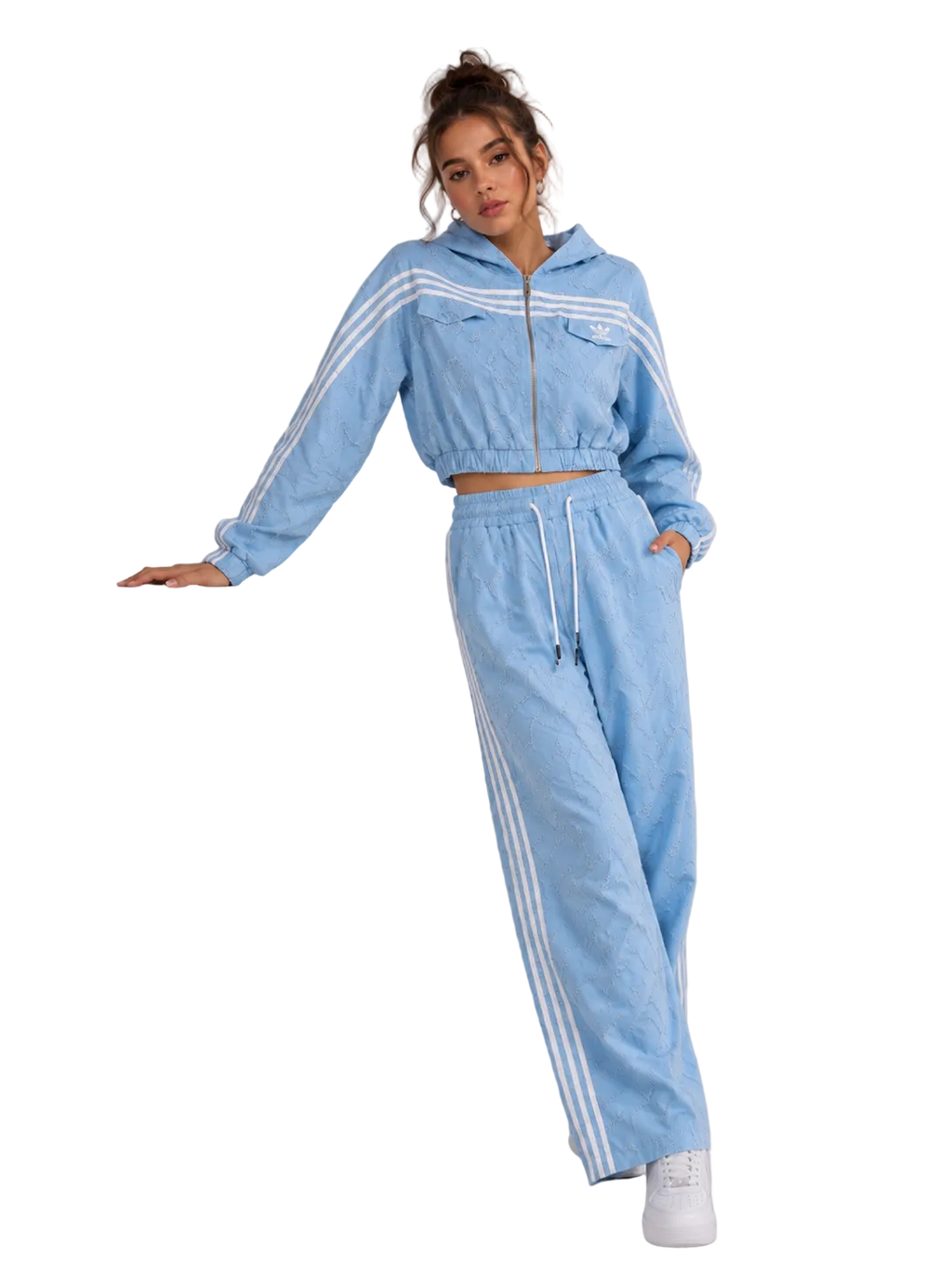 A woman models a light blue two-piece tracksuit featuring a cropped zip-up hoodie with white stripes and matching wide-leg sweatpants with white side stripes, posing next to a white display block.