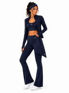 A woman modeling a matching navy blue activewear set consisting of a long-sleeve zip cardigan, sports bra, and high-waisted flared leggings, along with a matching headband and white sneakers, against a plain white background.