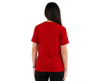A woman viewed from behind wearing a solid red short-sleeve crewneck t-shirt and black pants, standing against a plain light gray studio background.