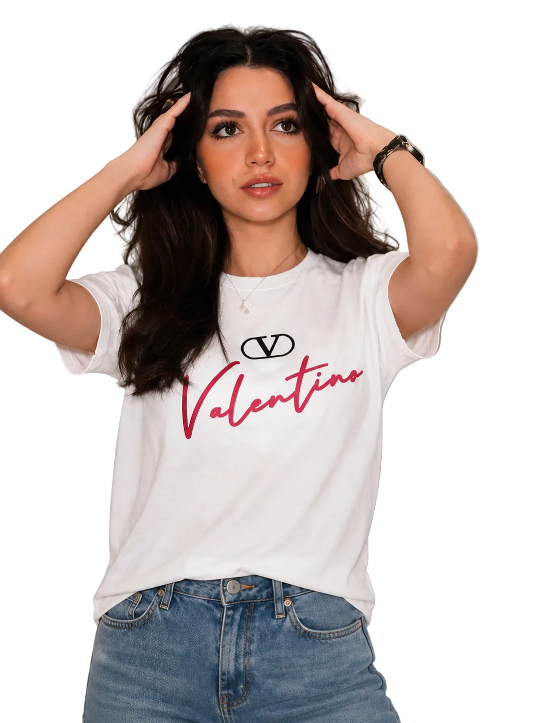 A woman wearing a white short-sleeve graphic t-shirt with a black Valentino logo and red script text, paired with blue jeans, posing against a light gray paneled wall.