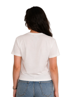 A woman viewed from behind wearing a plain white short-sleeve crewneck t-shirt and blue jeans, standing against a light beige paneled wall.