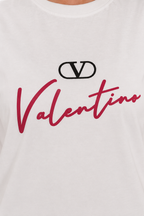 Close-up of a white Valentino T-shirt featuring a black interlocking V logo above the word 'Valentino' in red script across the chest.