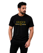 A man wearing a black Gucci t-shirt with a yellow logo and green and red double G emblem on the chest, posed against a neutral gray studio background.