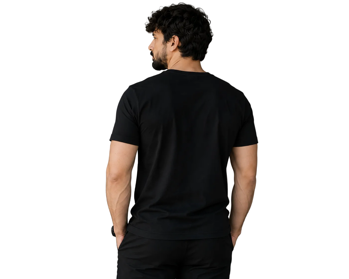 A man viewed from behind wearing a plain black short-sleeve crewneck t-shirt and black pants, standing in a modern indoor setting with a gray wall and a potted plant.