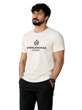 A man wearing a white Balenciaga Paris t-shirt with a black graphic logo on the chest, paired with black pants, standing in front of a modern gray wall.