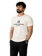 A man wearing a white Balenciaga Paris t-shirt with a black graphic logo on the chest, paired with black pants, standing in front of a modern gray wall.