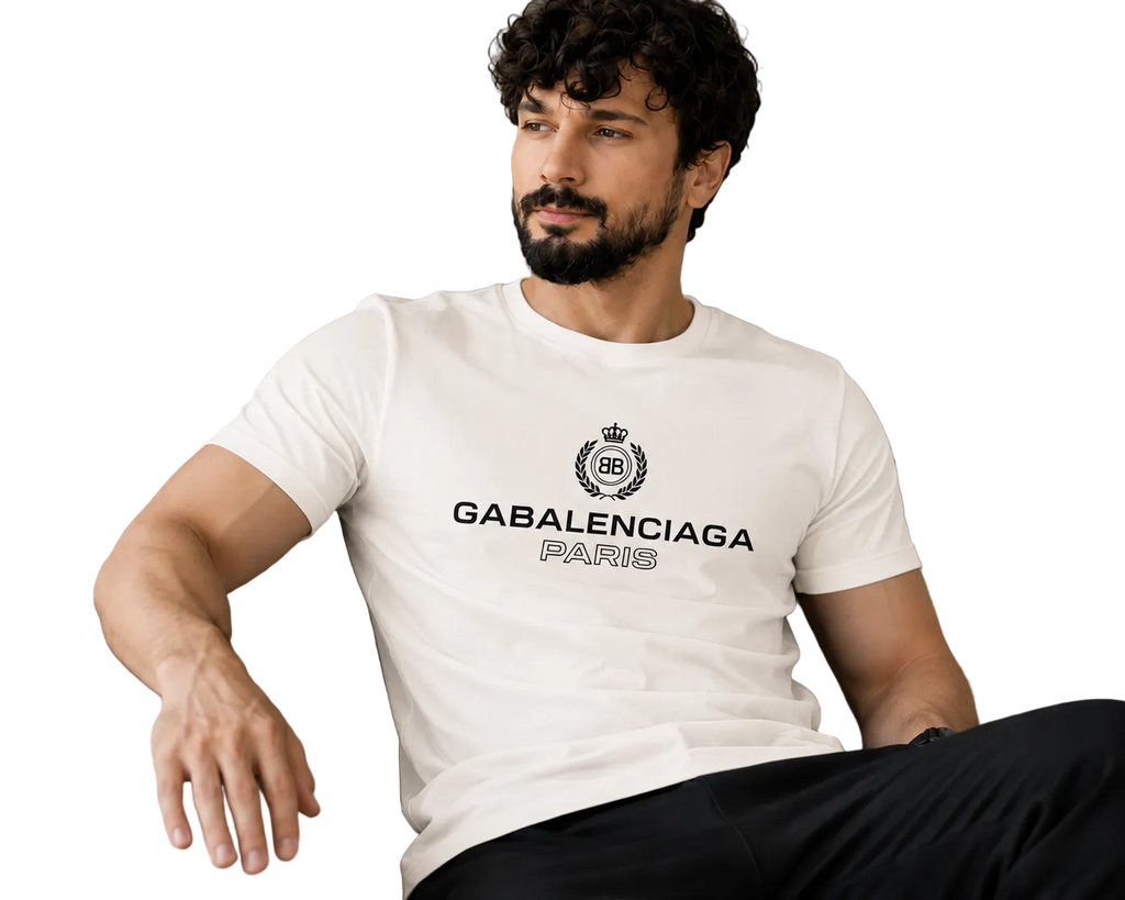 A man with a beard and curly hair sits on a beige couch wearing a white t-shirt with a black GABALENCIAGA logo and text on the chest.
