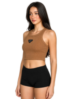 A woman modeling a brown ribbed knit crop top with a small black triangular logo patch on the chest, paired with black athletic shorts, against a neutral gray studio background.