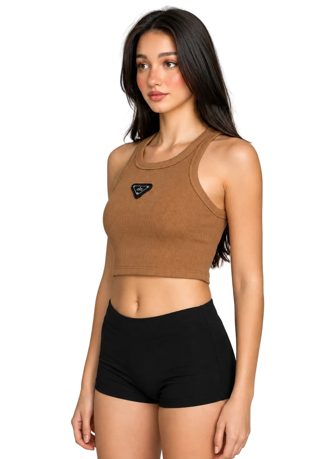 A woman modeling a brown ribbed knit crop top with a small black triangular logo patch on the chest, paired with black athletic shorts, against a neutral gray studio background.