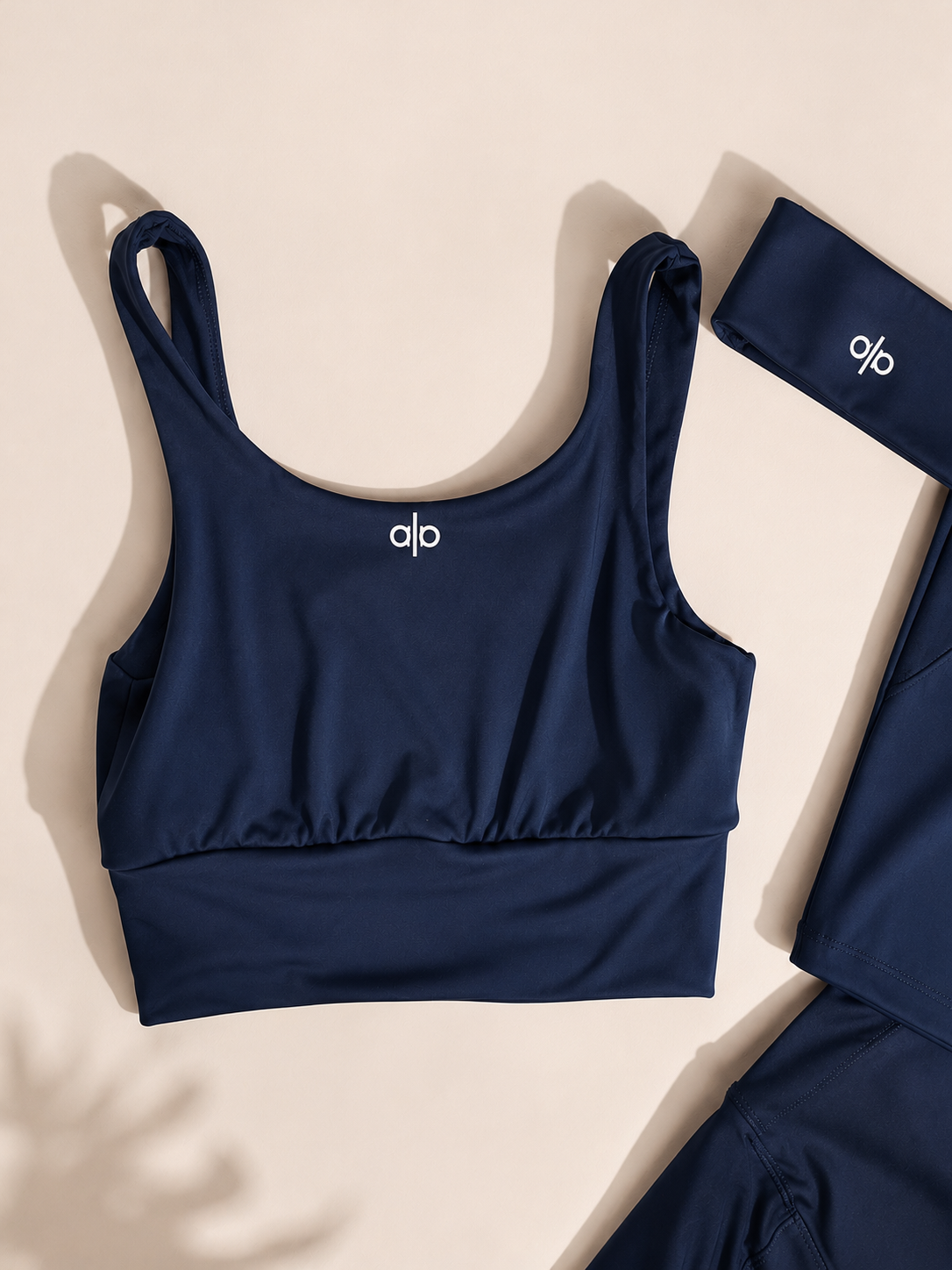 A navy blue high-waisted bikini bottom laid flat on a warm beige background, with matching navy swimwear pieces partially visible at the edges. A small white circular logo is printed on the front center and one leg band.