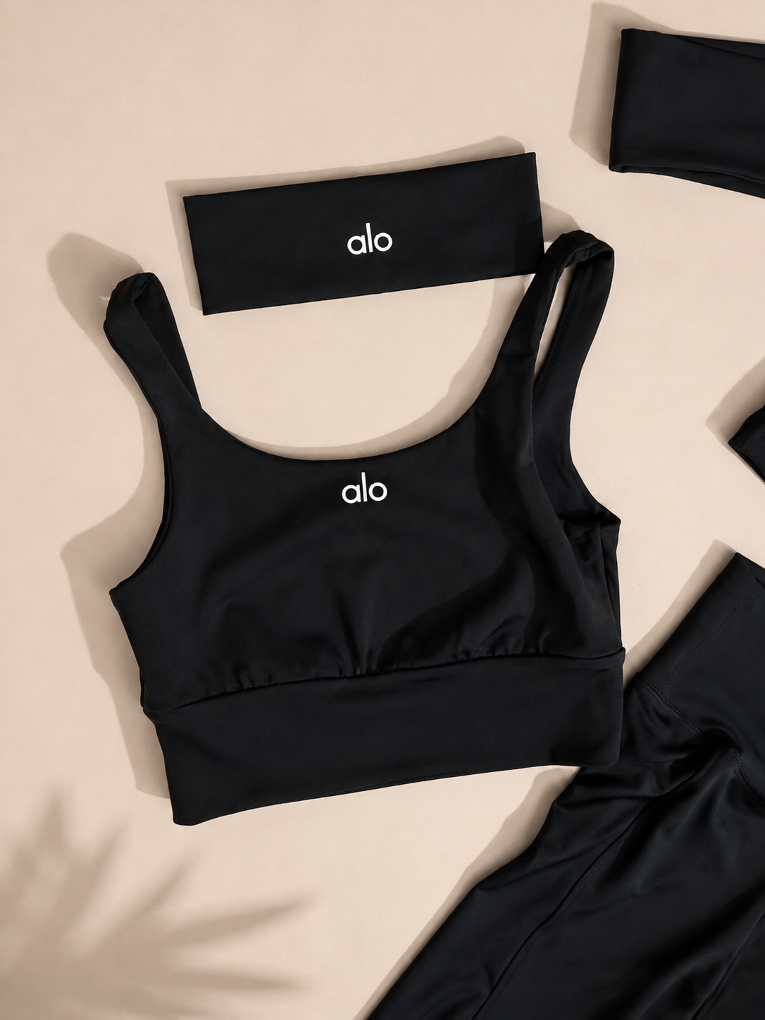 Black athletic bottoms set with a wide waistband, matching black headband, and cropped black fabric pieces, arranged on a light beige background. A small white 'oio' logo is visible on the main garment and headband.