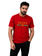 A man wearing a red short-sleeve Gucci t-shirt with a yellow and green logo graphic on the chest, paired with black pants, against a plain gray studio background.