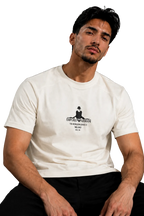 A man wearing a white crew-neck t-shirt with a black graphic print on the chest, seated in a black leather chair against a gray background.