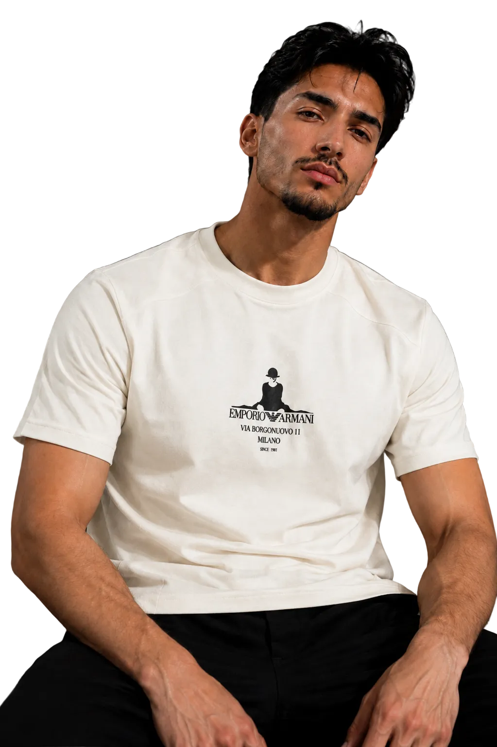 A man wearing a white crew-neck t-shirt with a black graphic print on the chest, seated in a black leather chair against a gray background.