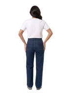 A woman viewed from behind wearing a white short-sleeve t-shirt and dark blue straight-leg jeans, standing against a plain white studio background.