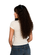 A woman with long, curly dark brown hair is shown from behind, wearing a fitted off-white short-sleeve t-shirt and blue jeans in a modern living room setting.