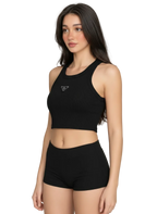 A woman modeling a black ribbed athletic crop top and matching high-waisted shorts against a plain light gray studio background.