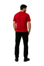 A man viewed from behind wearing a solid red short-sleeve t-shirt and black pants, standing against a neutral gray studio background with soft shadows.