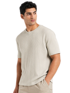 A man wearing a light beige short-sleeve crewneck knit shirt with vertical textured stripes, paired with matching beige trousers, set against a plain white background.