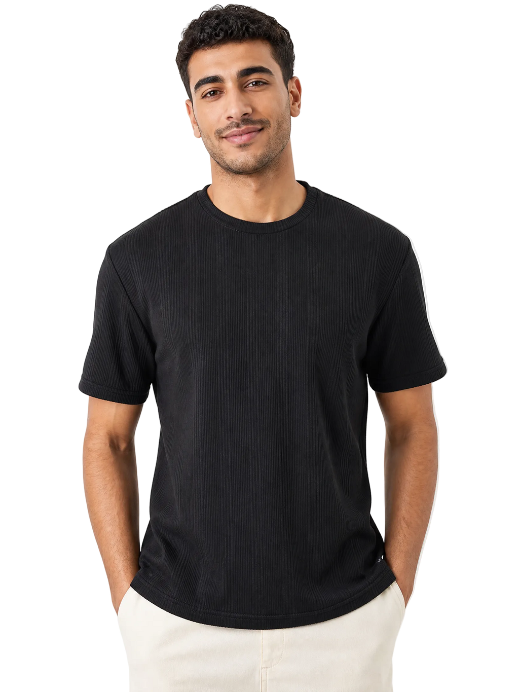 A man wearing a black short-sleeve ribbed crewneck t-shirt and off-white pants, standing against a solid white background.