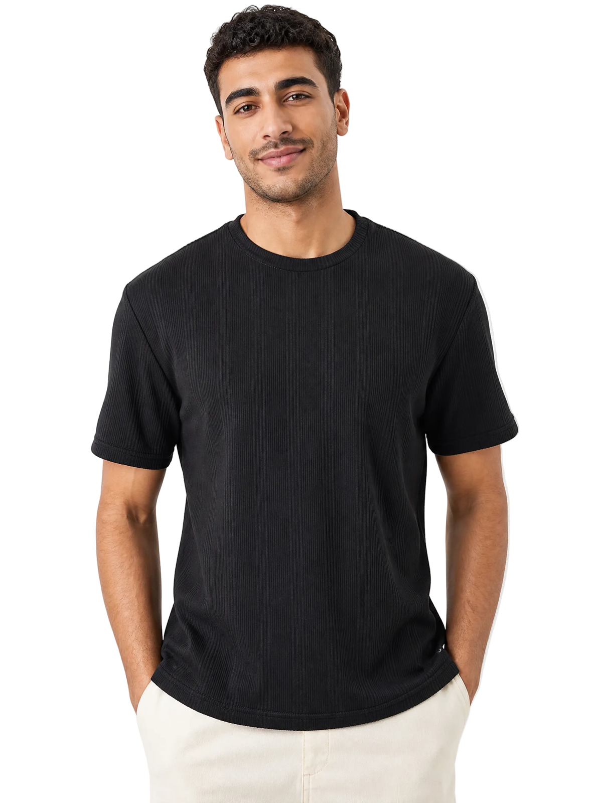A man wearing a black short-sleeve ribbed crewneck t-shirt and off-white pants, standing against a solid white background.