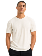 A man wearing a ribbed short-sleeve crewneck t-shirt in off-white, paired with black pants, photographed against a solid white background.