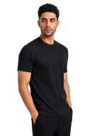A man wearing a black short-sleeve ribbed crewneck t-shirt and black pants, standing against a solid white background.
