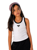 A young girl with long dark hair wearing a white tank top with black trim, a black Prada triangle necklace, and a patterned headband, posing against a plain light beige wall.