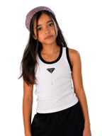 A young girl with long dark hair wearing a white tank top with black trim, a black Prada triangle necklace, and a patterned headband, posing against a plain light beige wall.