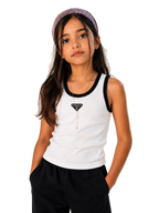 A young girl wearing a white tank top with black trim and a black triangle logo on the chest, paired with black pants and a patterned headband, posing against a light beige background.