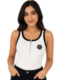 A woman modeling a white ribbed tank top with black trim, a half-zip neckline, and a black hexagonal logo patch on the left chest, paired with black jeans against a plain white background.