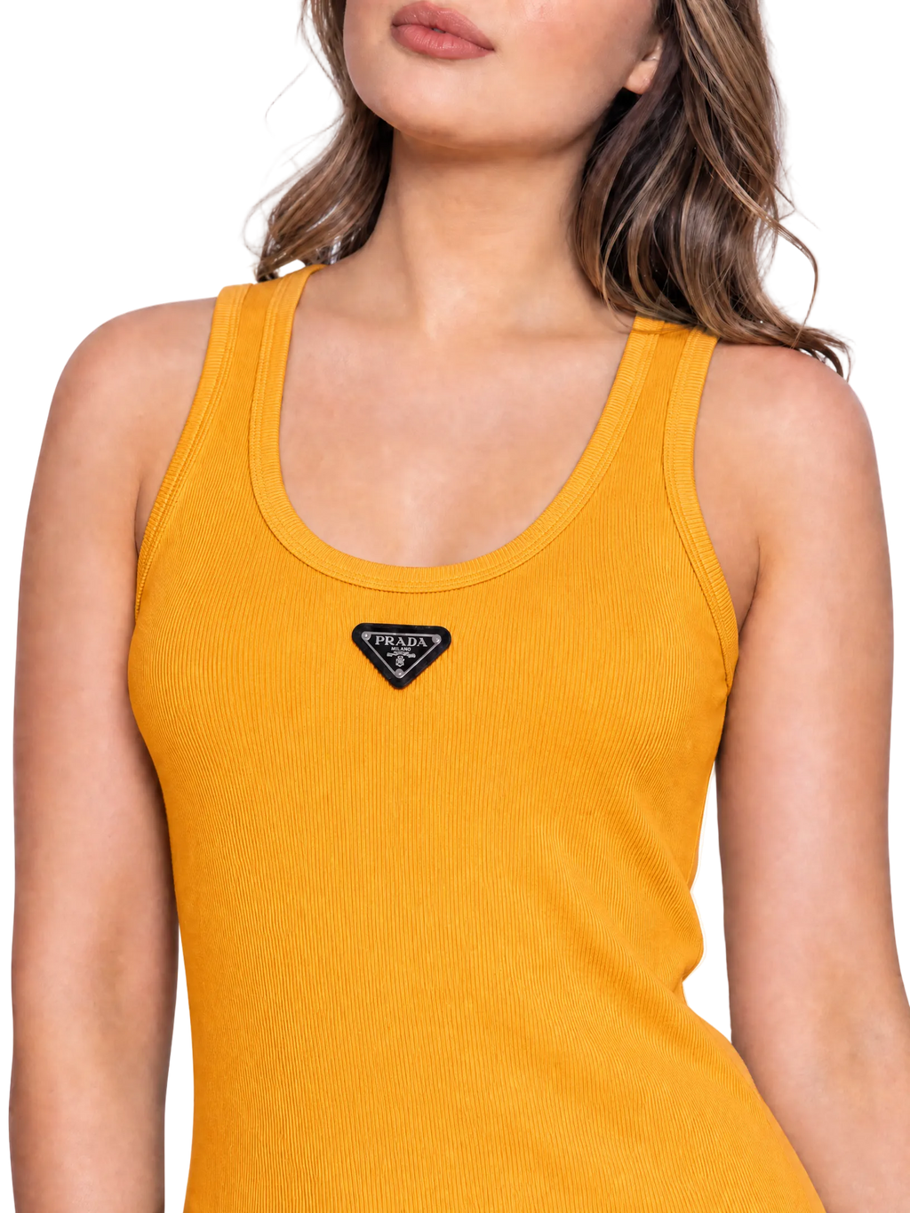 A close-up of a woman wearing a ribbed yellow tank top with a small black triangular Prada logo patch on the chest, against a clean white background.