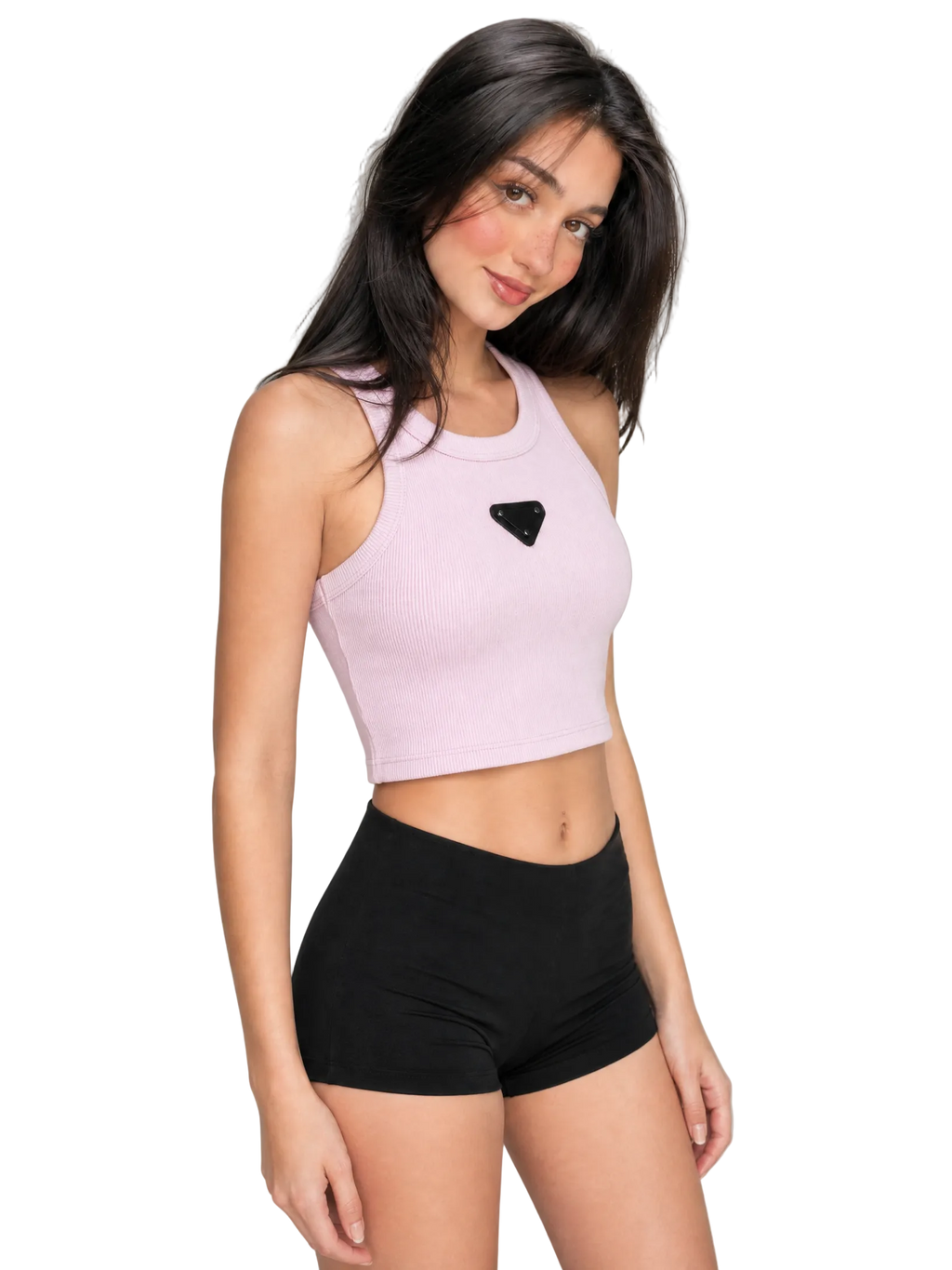 A woman modeling a light pink ribbed crop top with a black triangular logo patch on the chest, paired with black athletic shorts, against a neutral gray background.