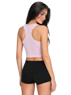A woman shown from the back wearing a light pink racerback crop top and black athletic shorts, standing against a neutral light gray studio background.