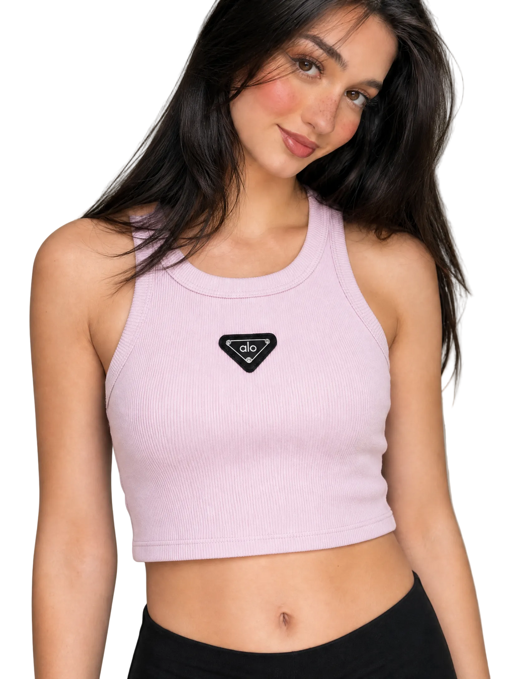A woman wearing a light pink ribbed crop top with a black triangular patch on the chest, paired with black bottoms, against a neutral gray background.