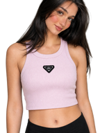 A woman wearing a light pink ribbed crop top with a black triangular patch on the chest, paired with black bottoms, against a neutral gray background.