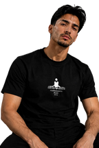 A man wearing a black short-sleeve t-shirt with a white graphic print on the chest, sitting in a black leather chair against a gray background.