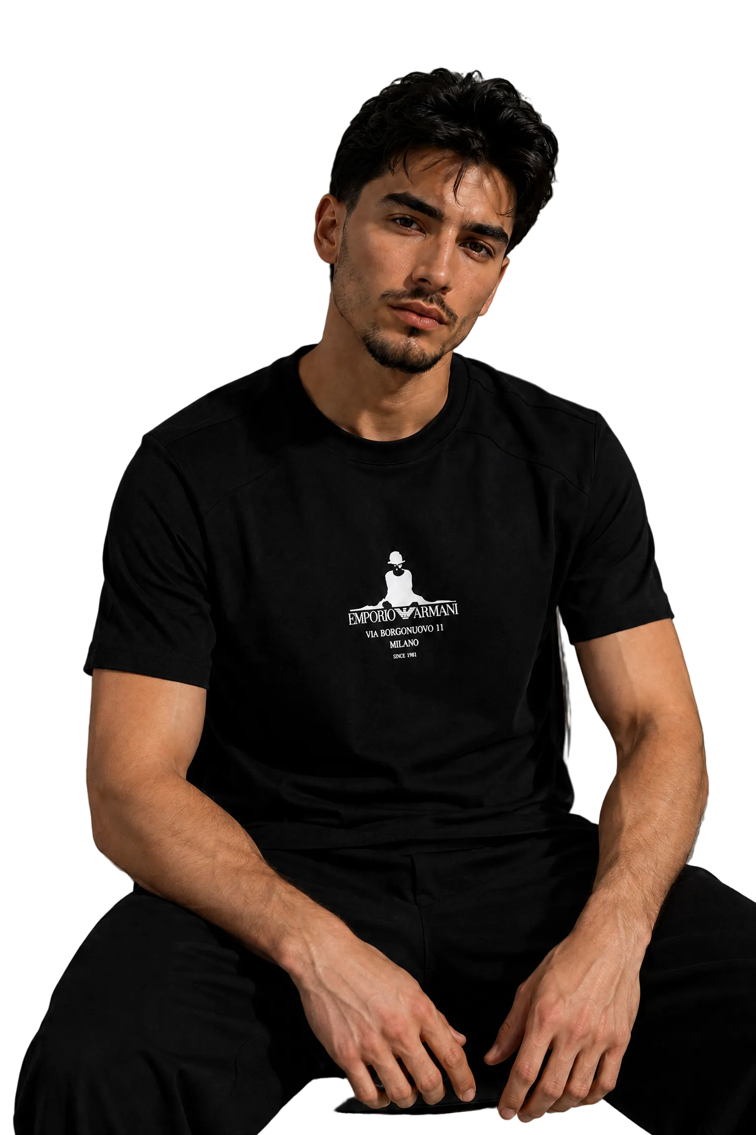 A man wearing a black short-sleeve t-shirt with a white graphic print on the chest, sitting in a modern room with a gray wall and a black leather sofa in the background.